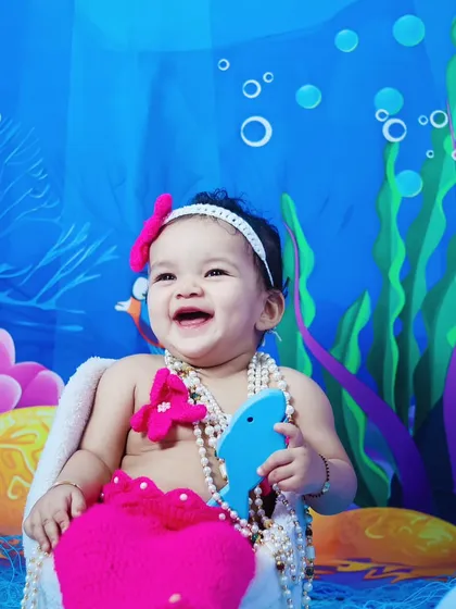 A joyful baby girl laughing during her pink mermaid-themed photoshoot.