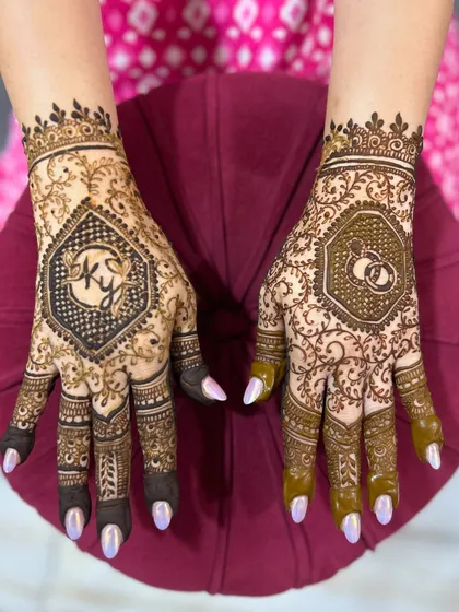 A personalized engagement mehendi featuring the couple's initials 'KY' on one hand and a motif of interlocking wedding rings on the other.