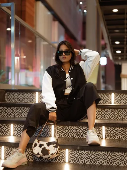 A cool, relaxed portrait on a set of illuminated stairs. The model's varsity jacket and casual pose give this a modern, laid-back street style vibe.