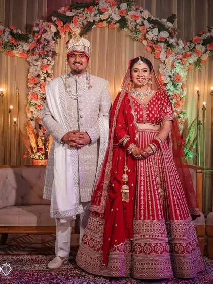 A classic stage portrait of the couple, smiling for the camera against a beautifully decorated floral arch.