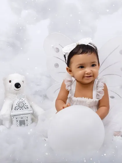 A sweet portrait of a baby girl dressed as an angel, sitting with a polar bear prop in a dreamy cloud setup.