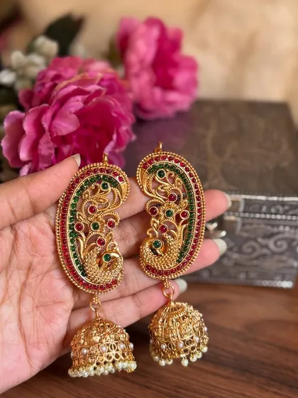 A pair of beautiful peacock-motif earrings with red and green enamel work and jhumka drops. These can be worn as standalone statement earrings.