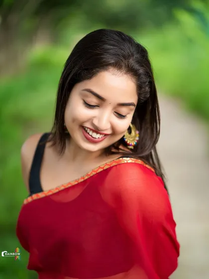 A candid moment captured in a sheer red saree. The model's downward glance and natural smile give this portrait an intimate and gentle feel.