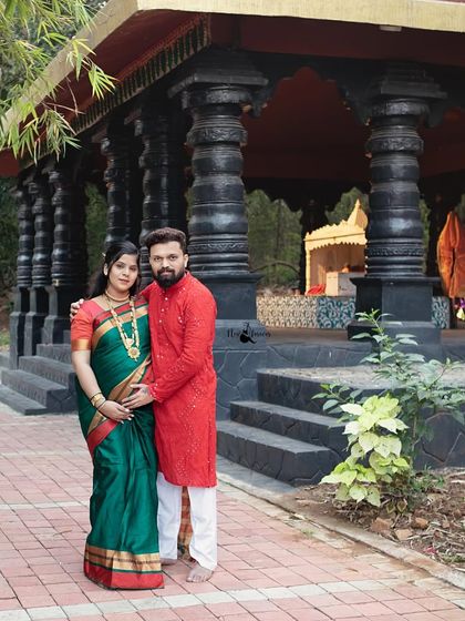 A beautiful full length portrait of the couple at a location with traditional architecture. This shot showcases their coordinated ethnic outfits and the serene setting of their cultural maternity shoot.