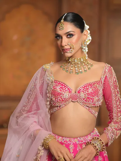 A full view of the bride in her vibrant pink lehenga. The long, gajra-adorned braid adds a touch of traditional grace to this modern, colorful look.
