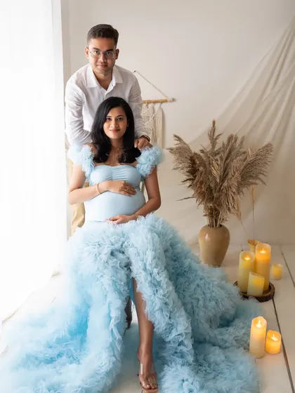 A lovely portrait of the couple in a boho-inspired setup. She is seated in the blue gown, surrounded by pampas grass and candles, creating a warm and stylish look.