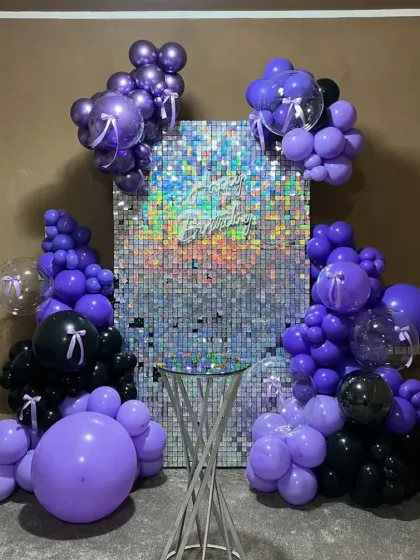 A bold birthday setup with a silver sequin wall framed by purple and black balloons.