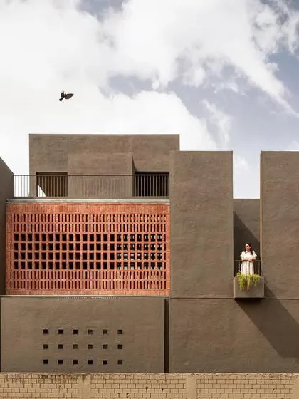 The west-facing facade of the 'H-House' features a crafted brick screen that filters the harsh sun, creating shifting shadows while ensuring privacy.