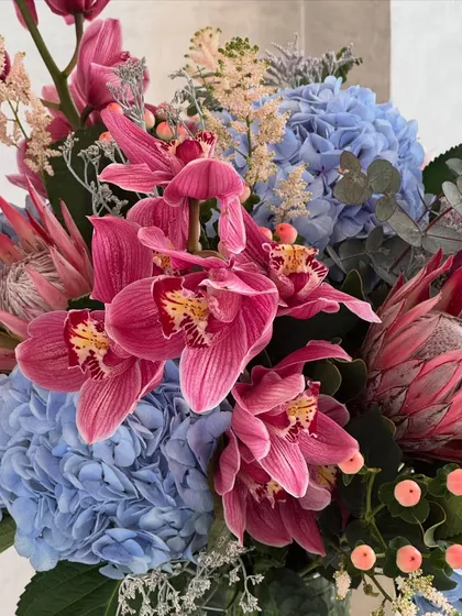 Just some pretty flowers in a crystal vase. Can you name them all? This close-up shows the beautiful pairing of blue hydrangeas, pink cymbidium orchids, and exotic protea.