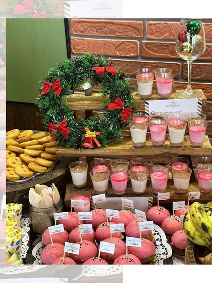 A festive dessert table for a Christmas party, featuring mini burgers with pink buns, dessert shots, and a wreath for a touch of holiday cheer.