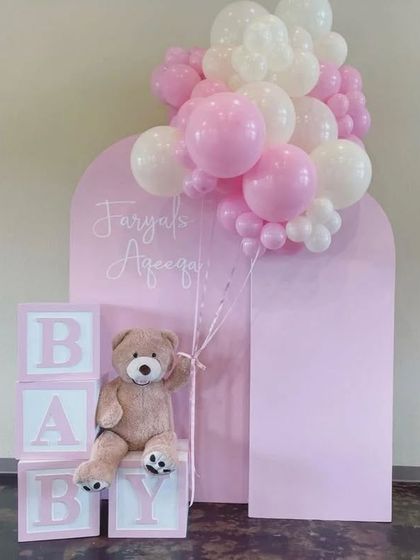 A sweet and simple baby welcome or Aqeeqah ceremony decor in pink and white, with "BABY" blocks and a teddy bear prop.