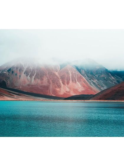 A moody, atmospheric shot of Pangong Lake, with low clouds shrouding the colorful, mineral-rich mountains.