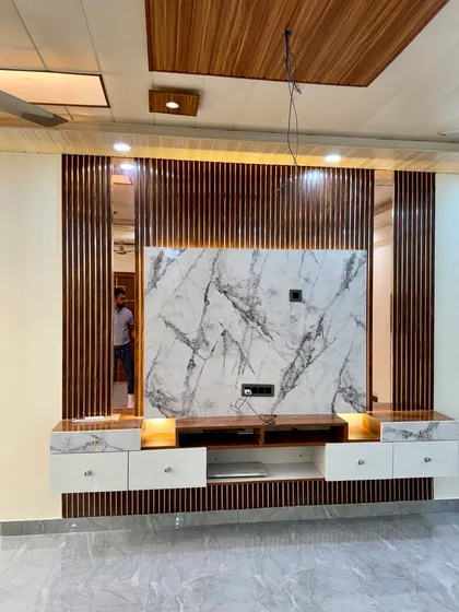 A grand TV unit design with a large marble panel at the center, flanked by mirrors and wood-fluted panels. The white and wood-finish console offers ample storage.
