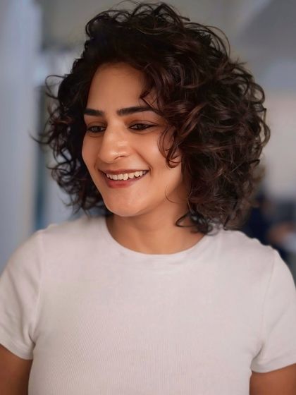 A happy client showing off her new short curly bob. This cut is designed to be low-maintenance while still looking effortlessly chic.