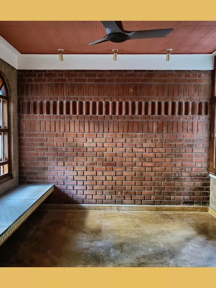 An empty room with a built-in window seat, showcasing the texture of the soil cement blocks and a unique perforated brick detail for ventilation.
