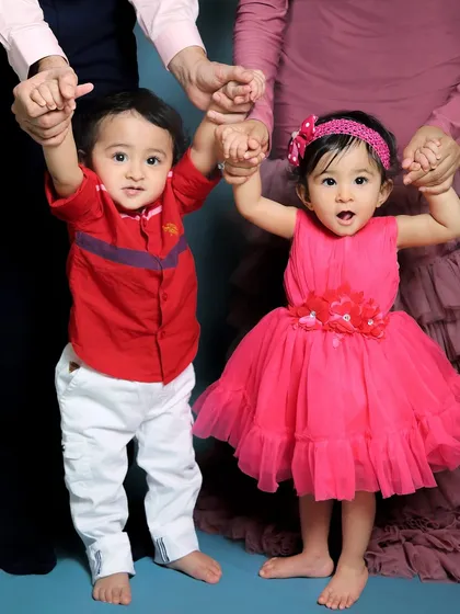 A close-up on the one-year-old twins from a family photoshoot. Holding their parents' hands, they are ready to take on the world together.