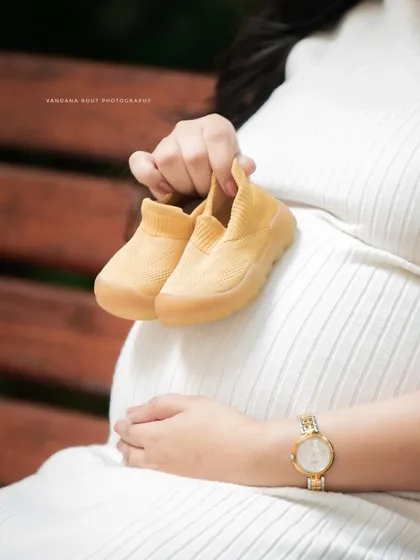 A close-up detail shot focusing on a tiny pair of baby shoes held against the mother's bump. Sometimes the smallest props tell the biggest story.