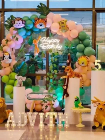 A fun jungle animal theme with many plush toys and cutouts. This setup includes a balloon arch with animal head foils, a 'Happy Birthday' neon sign, and light-up letters, creating an immersive jungle experience.