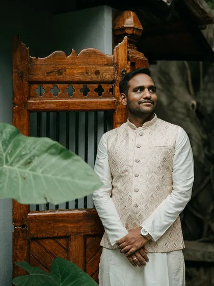 The groom, in a classic ivory vest, stands beside a carved wooden door, a picture of timeless elegance.