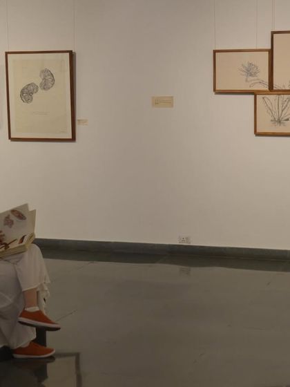 A visitor sits and reads through one of the artist's books at 'Bring me Flowers', demonstrating the quiet, interactive nature of the show.