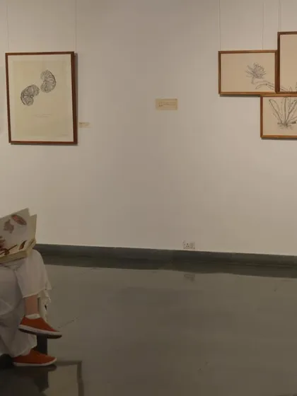 A visitor sits and reads through one of the artist's books at 'Bring me Flowers', demonstrating the quiet, interactive nature of the show.