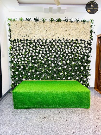 A simple and elegant floral wall we created for a home event. This backdrop features a mix of white flowers and green leaves, with a turf-covered base that can be used for seating.