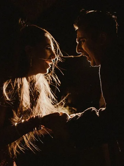 A dramatic, low-light shot capturing the playful energy between the couple. The rim lighting creates a beautiful silhouette, highlighting their expressions and connection.
