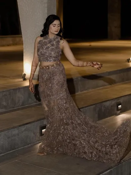 A stunning, full-length shot of a Sangeet look. The bride's embellished gown flows beautifully as she descends the stairs, her soft waves and glowing makeup completing the picture of modern grace.