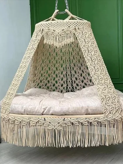 A beautiful leaf-patterned macrame swing in a natural, off-white color. The design is open and airy, perfect for a room with lots of plants and natural light.