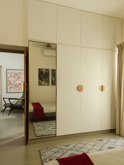 The master bedroom, designed with a calm palette of off-white and natural wood. A full-length mirror on the wardrobe door enhances the sense of space and reflects the light from the large window.