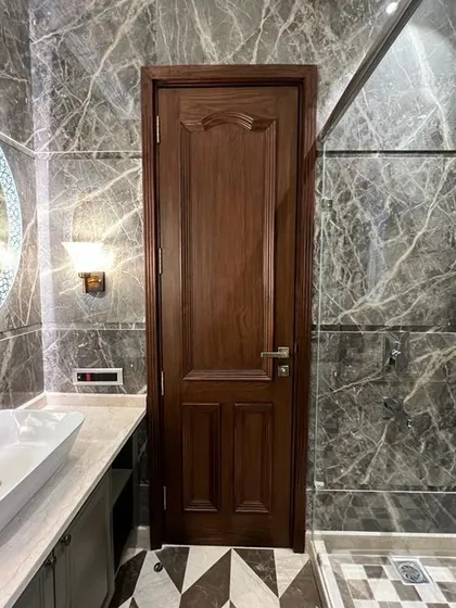 This bathroom combines dark grey marble walls with a striking checkerboard floor. The round, backlit mirror and classic wall sconces add a touch of timeless elegance.
