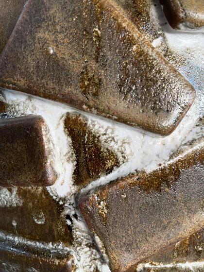A detailed shot of the same Moon Jar after firing. The glaze has melted and run, creating a rich, varied surface where the brown ceramic body shows through the white.