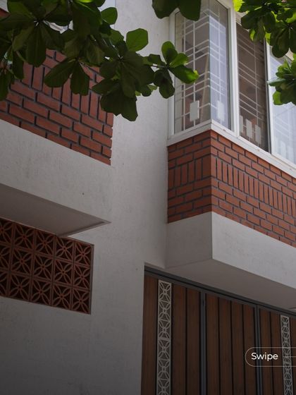 A detail of the facade showing the combination of white plaster, exposed brick, terracotta jali screens, and a wooden gate.