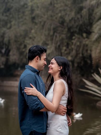 Sharing a look of love by a serene pond. The calm water and greenery enhance the peaceful, romantic mood of this outdoor couple photoshoot.