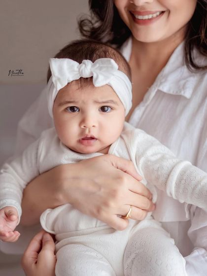 A close-up portrait of a beautiful baby girl in her mother's arms, looking right at the camera.
