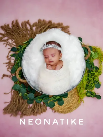 A simple and earthy newborn setup. The baby is wrapped in white and placed in a metal bowl on a bed of jute and greenery, creating a natural and rustic feel.