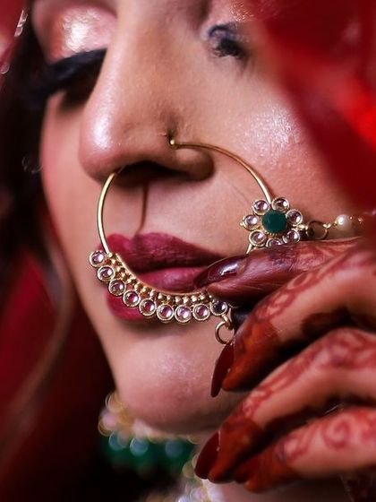 A detailed close-up of the bride, focusing on her expressive eyes and traditional nath. The red veil frames her face, creating an intimate and classic Indian bridal portrait.