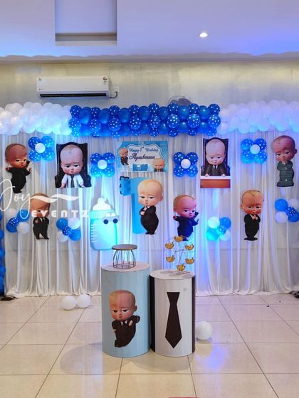 This Boss Baby decoration features a wide backdrop of white curtains accented with character cutouts and blue balloon arrangements. Themed plinths in the front are ready for the cake and desserts.