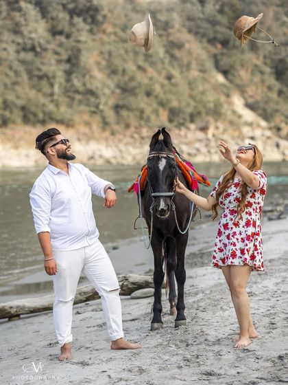 A playful and joyful moment as the couple throws their hats in the air during their beach pre-wedding shoot with a horse.