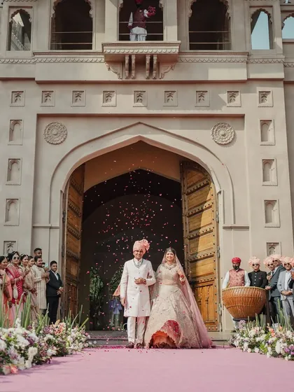 A grand entrance for the bride and groom at their Fairmont Jaipur wedding. The royal architecture and a path showered with petals make for a truly majestic moment.