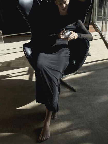 A person holds the Bocci 14p while sitting in a classic designer chair, illustrating the lamp's role as a personal, portable piece of design.