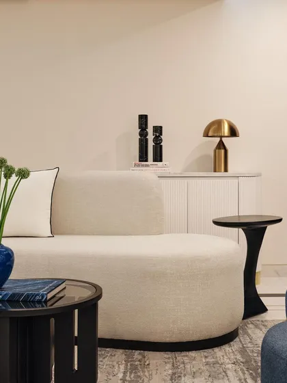 This living area is filled with warm tones and inviting textures. The space features a comfortable curved sofa, a sculptural black side table, and a fluted white console, creating a harmonious blend of modern shapes and soft materials.