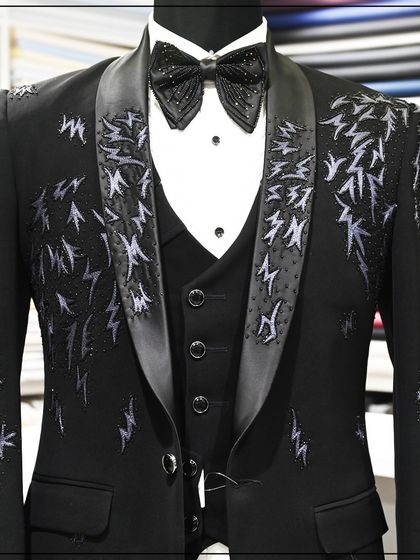 A close-up of the black tuxedo with abstract silver embroidery, showing the texture and detail of the threadwork.