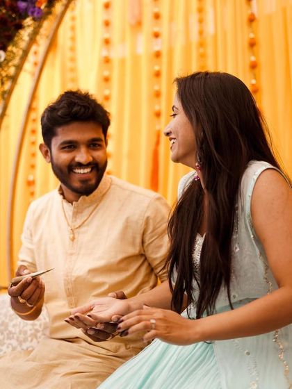 Candid moments from a Mehendi function. The decor features a simple yet elegant yellow curtain backdrop with floral details, perfect for a relaxed and intimate celebration.