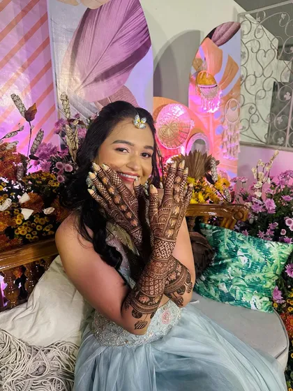 A happy, winking client showing off her beautiful, dense mehndi design, full of hearts and traditional patterns.