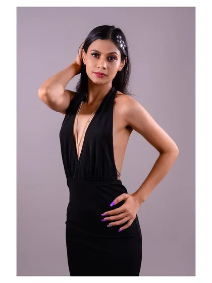 An elegant studio shot of a model in a black halter dress. The simple grey background ensures that the focus remains on the dress's plunging neckline and sleek silhouette.
