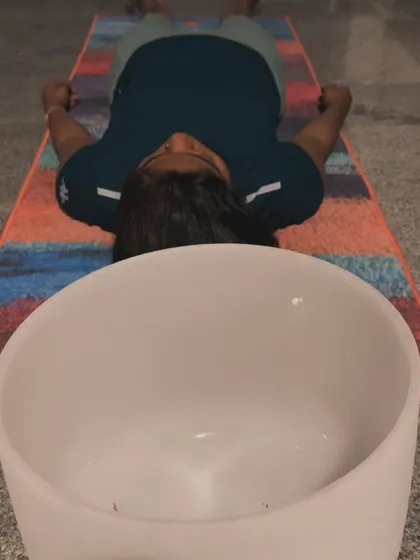 A close up view of a client experiencing deep rest during a sound bath. A large crystal singing bowl is placed nearby, its pure frequency helping to clear the mind and balance the body's energy, leading to a state of profound calm.