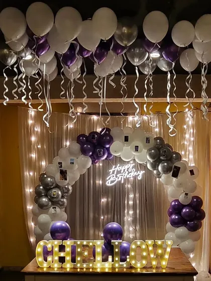 I can create more intimate, personalized setups as well. This table-top decoration features a balloon arch with small photos clipped on, a neon sign, and a light-up name, all set against a fairy light curtain.