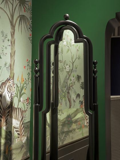 A custom-designed mirror with a traditional, ornate black frame, reflecting a vibrant, tropical-themed wallpaper. Our pieces are designed to complement and enhance their surroundings.
