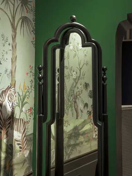 A custom-designed mirror with a traditional, ornate black frame, reflecting a vibrant, tropical-themed wallpaper. Our pieces are designed to complement and enhance their surroundings.